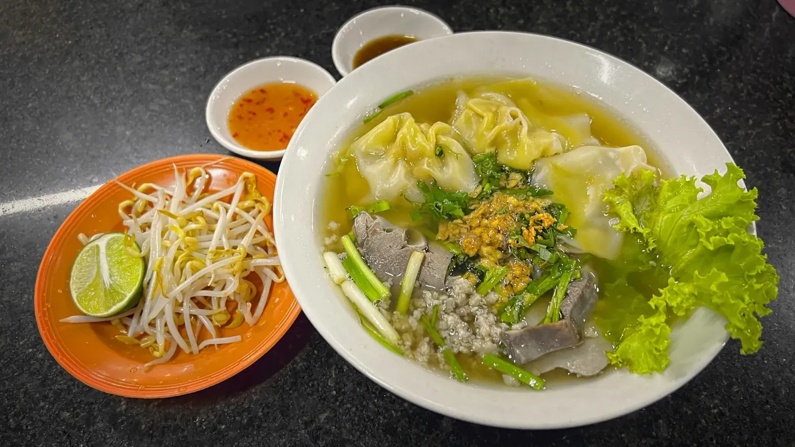 Kuy Teav by Mr. Wanderer Bowl of Kuy Teav with a side of bean sprouts and a lime wedge.
