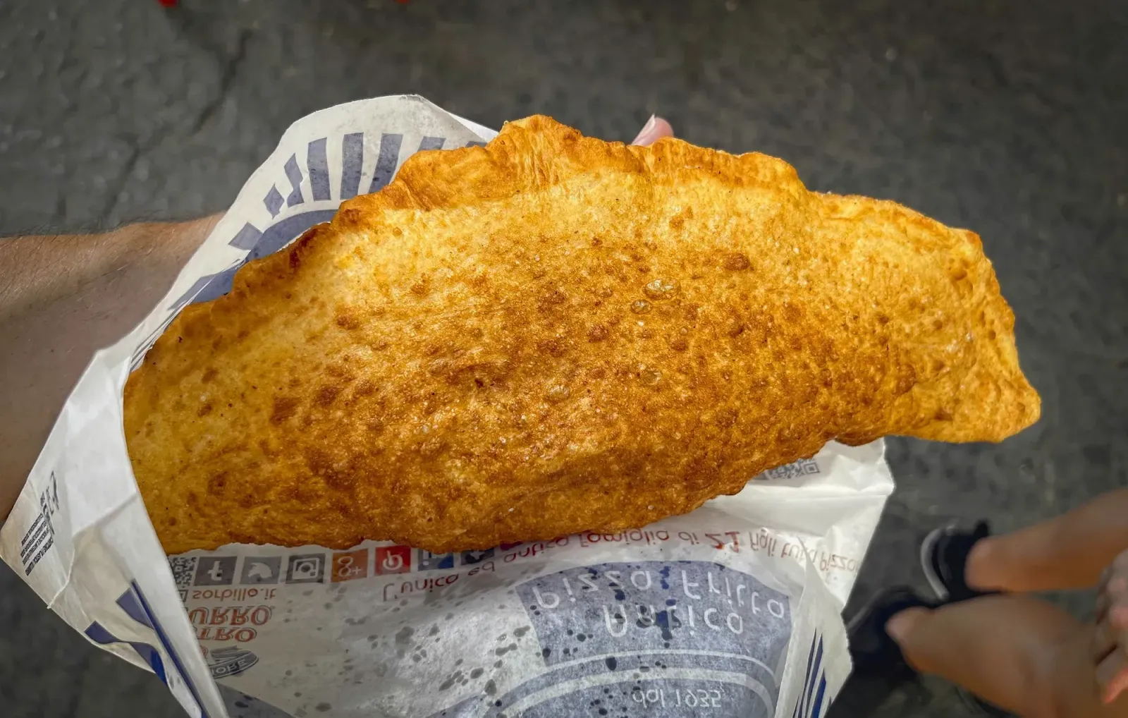 Fried Pizza by Mr. Wanderer Fried Pizza. Overhead shot holding street food fried pizza in hand.
