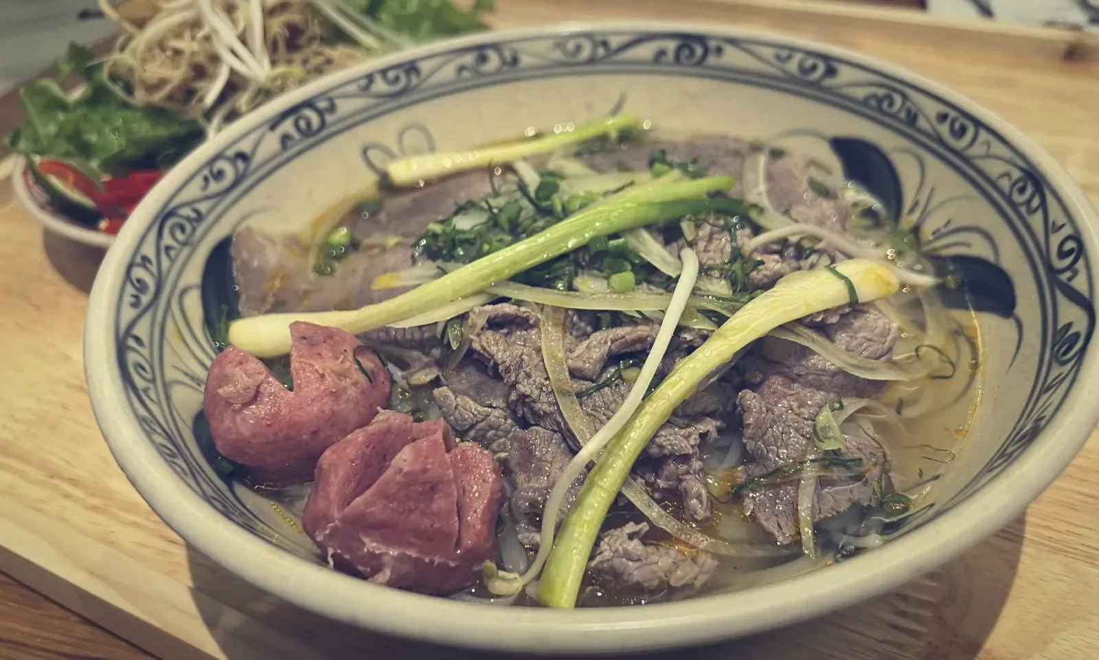 Bún bò Huế by Mr. Wanderer Bowl of Bún bò Huế with garnishes in the background.