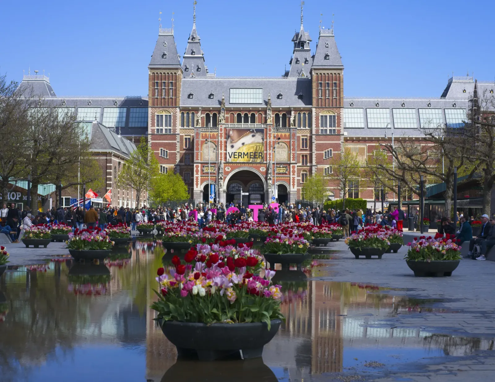 Rijksmuseum by Mrs.Wanderer Museum reflected in a pool of water with basins of tulips