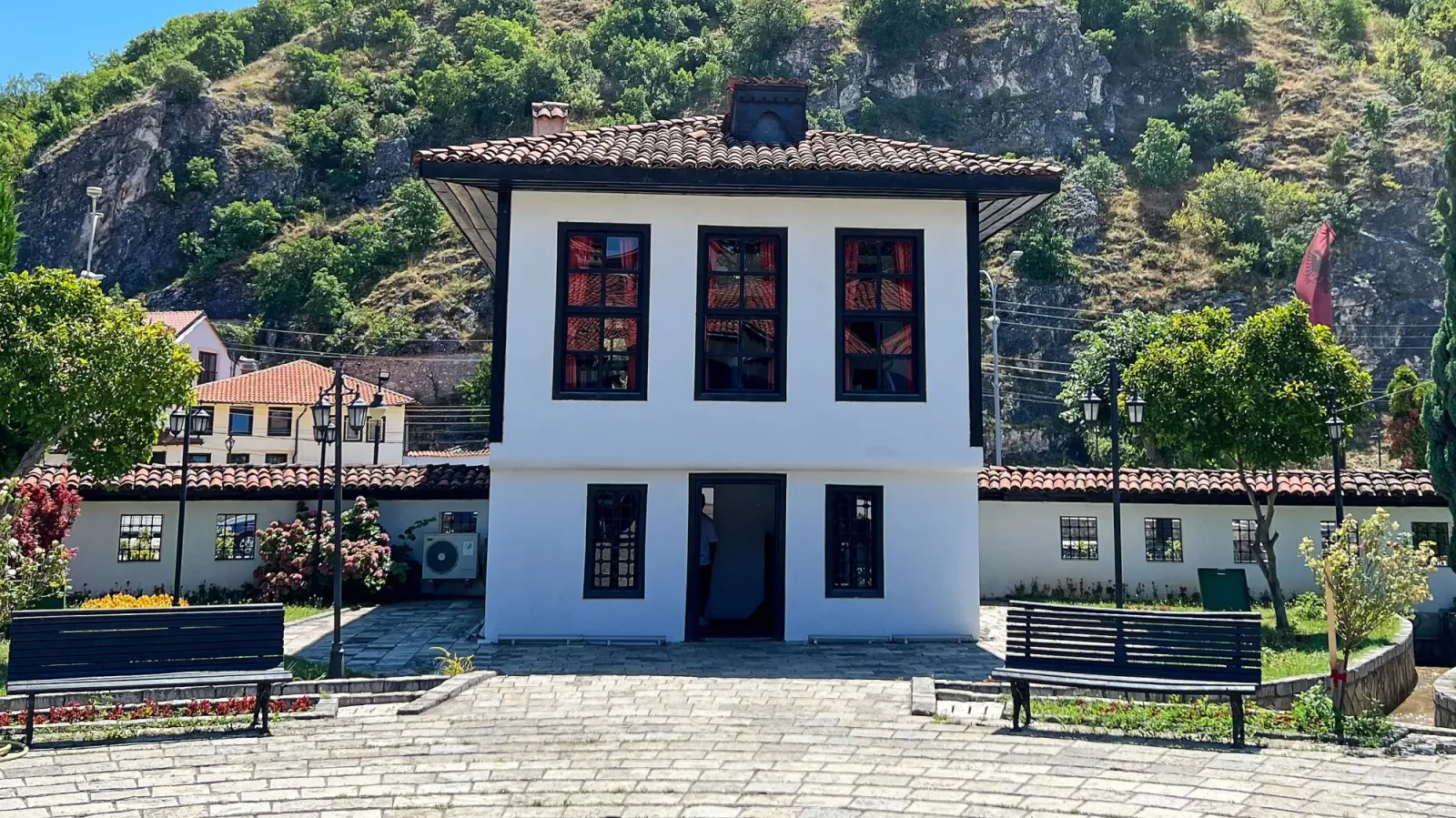 Albanian League of Prizren by Mrs. Wanderer White building with black windows set at the foot of a tree covered hill