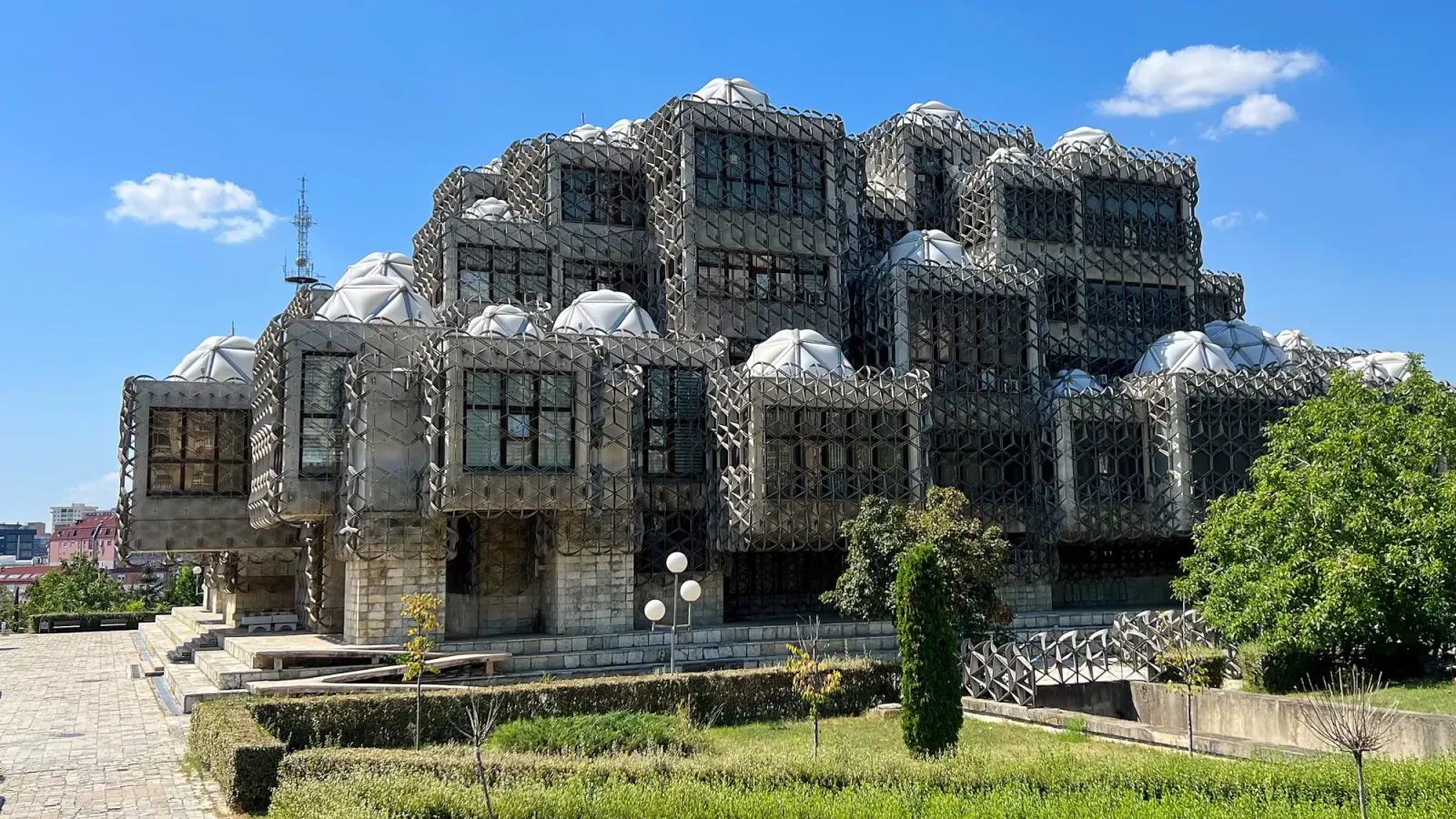 National Library of Kosovo by Mrs. Wanderer Grey concrete building covered in black mesh cages with white angular domes on top