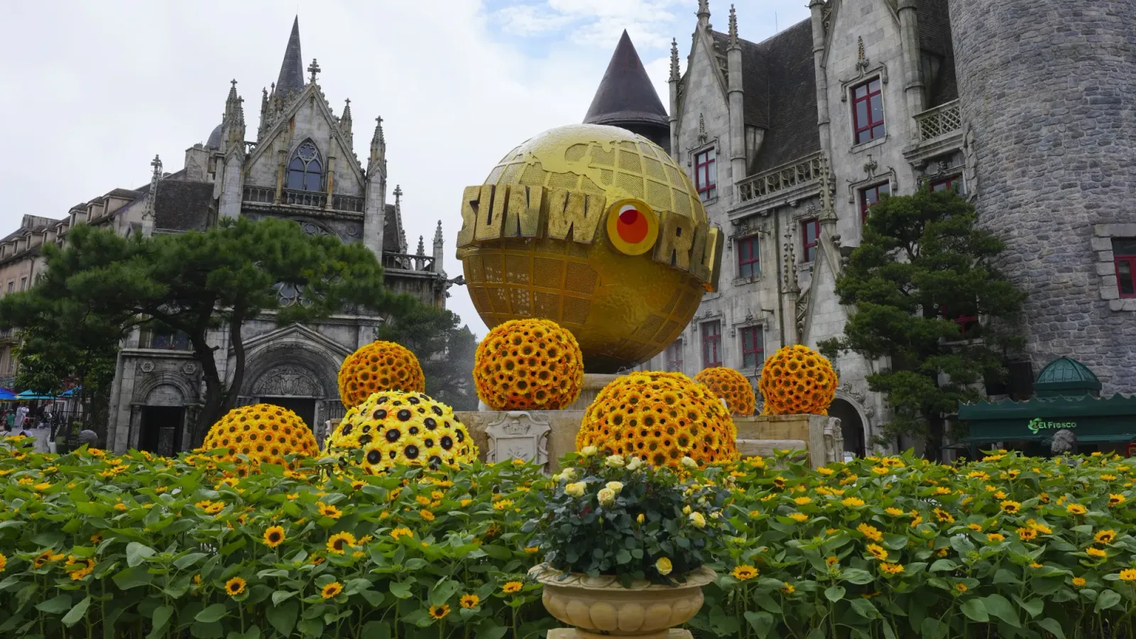 Sun World by Mr. Wanderer Golden Globe with "Sun World" written on it with sun flowers around it and a castle in the background