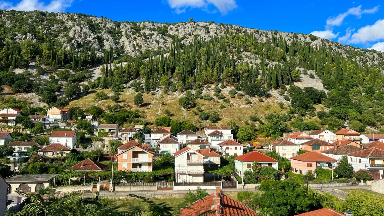 Bosnian Countryside by Mr. Wanderer Warm colored houses nestled into the foot of a grey stone mountain lined with trees