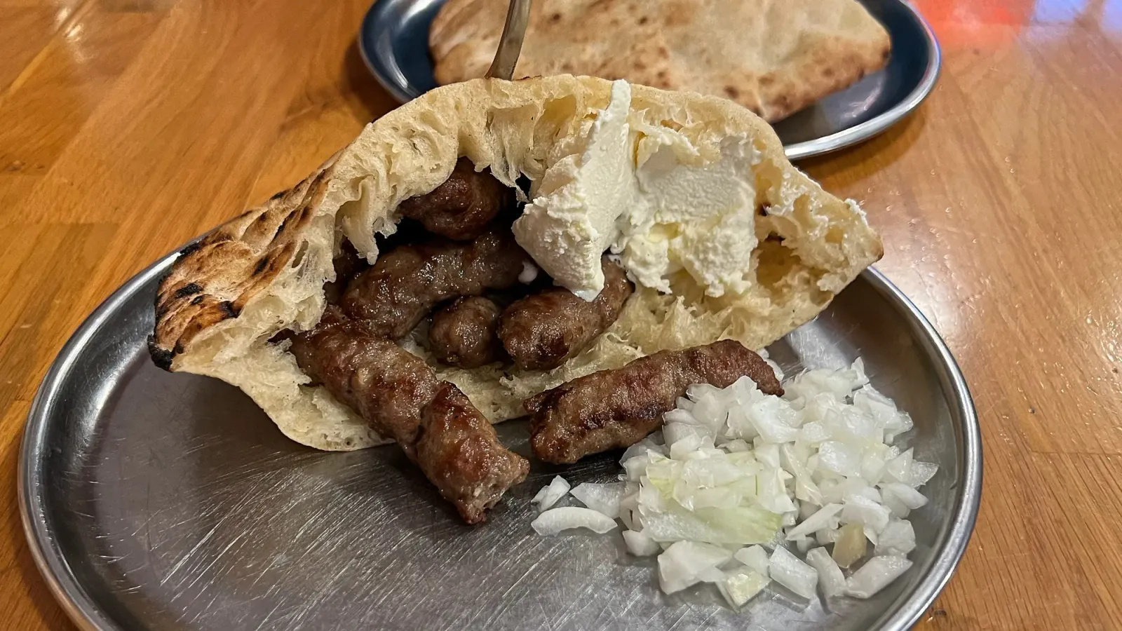 Cevapi with Kajmak by Mr. Wanderer Open bread pocked with meat, cheese, and onions on a silver plate