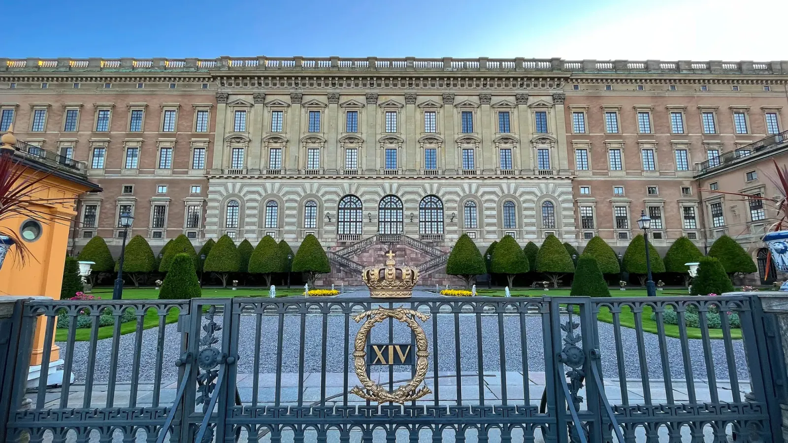 Kungliga Slottet by Mrs. Wanderer Heavily windowed facade with a black gate and golden crest in the forefront
