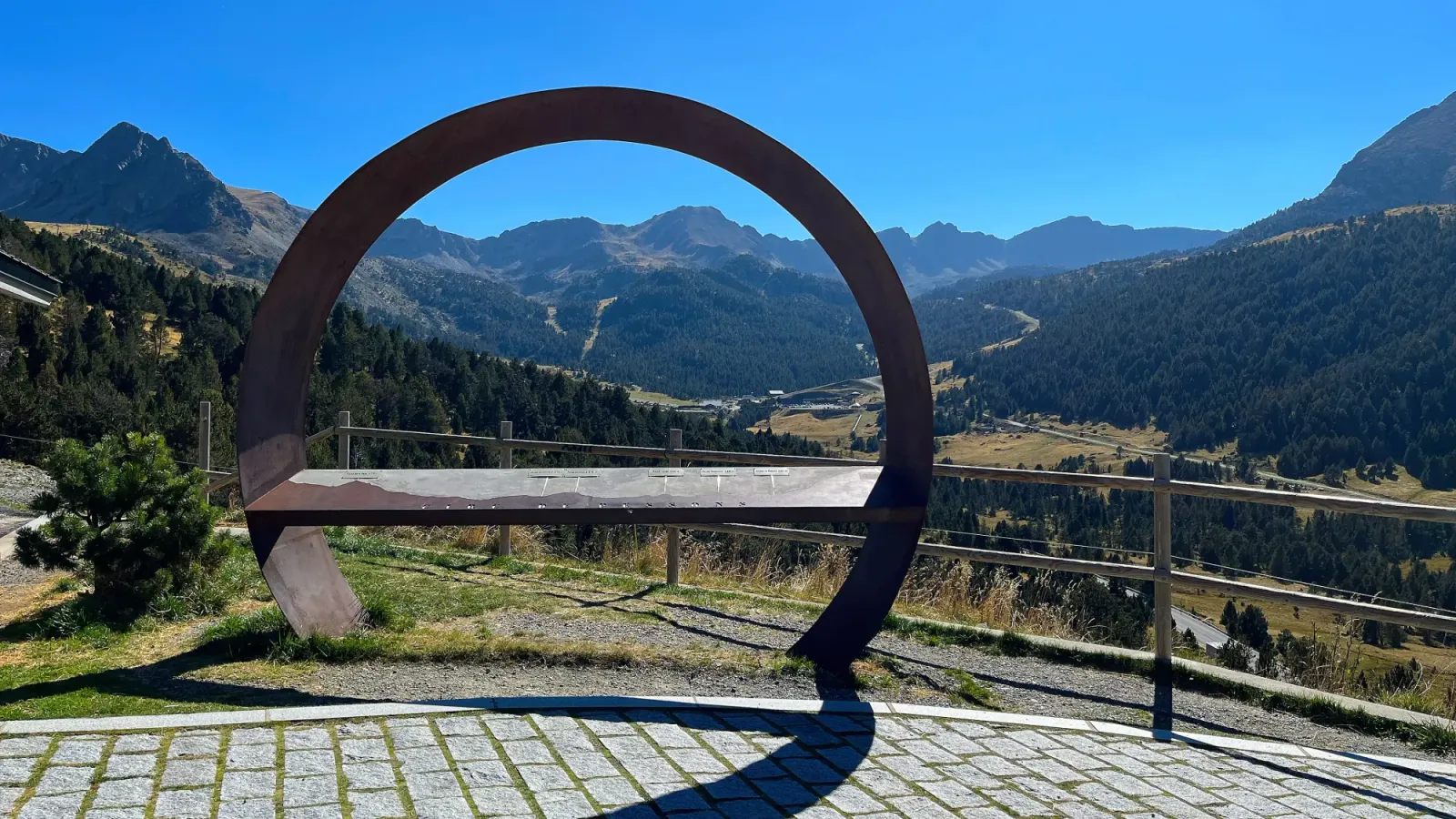 Andorra Vista by Mrs. Wanderer Round frame pointed out over a valley surrounded by mountains