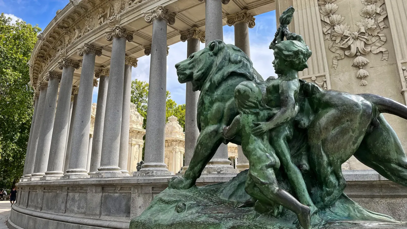 Parque de El Retiro by Mrs. Wanderer Statue of a lion and two children in front of a curved row of columns