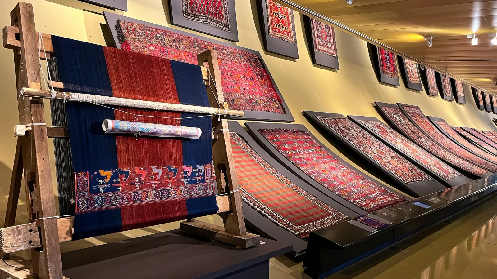 Baku Carpet Weaving by Mrs. Wanderer A loom in progress alongside a wall full of mounted woven carpets