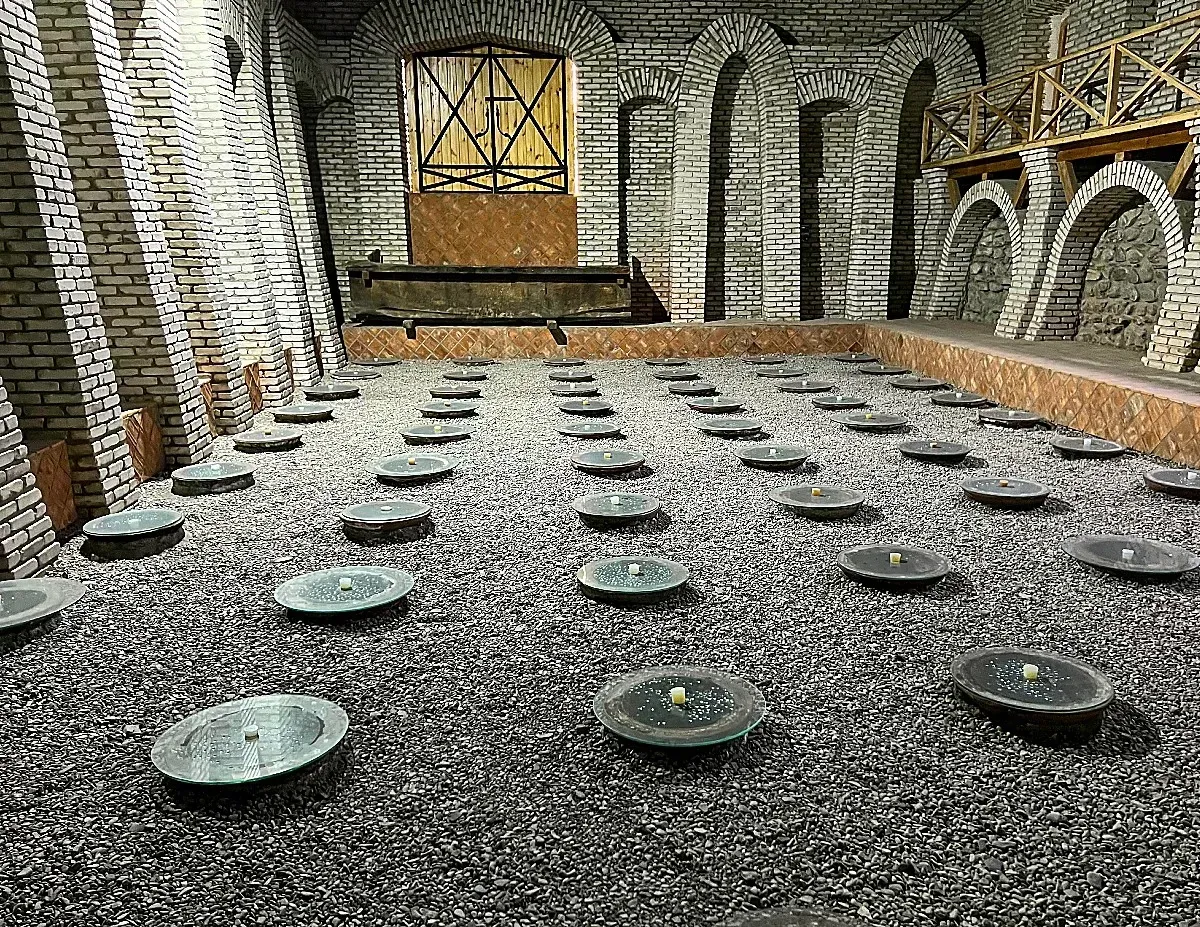 Wine Jars by Mr. Wanderer Dozens of round lids sitting on clay wine jugs burried under a gravel floor in a white brick rooom