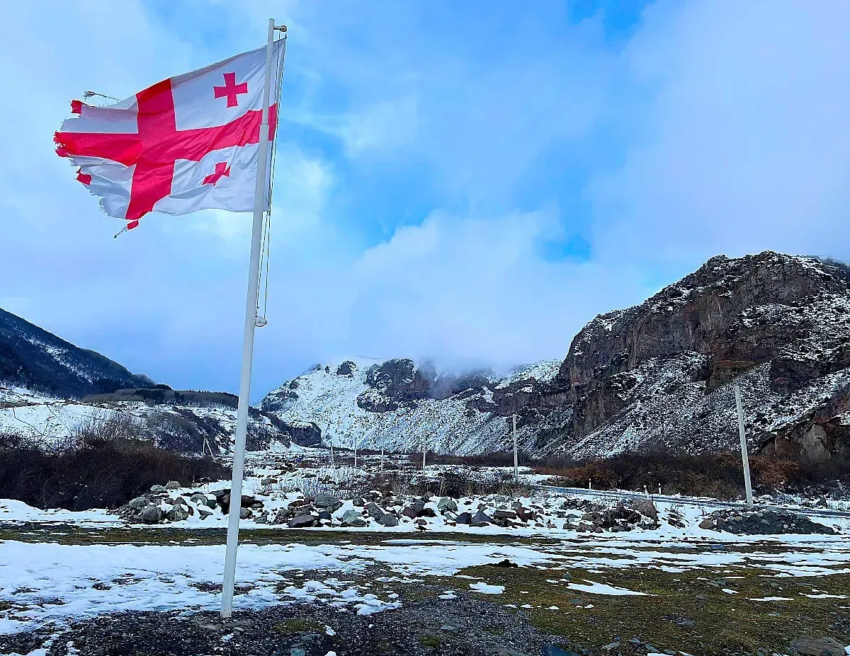 Wintery Georgia by Mrs. Wanderer Tattered Georgian flag blowing before snowy mountains