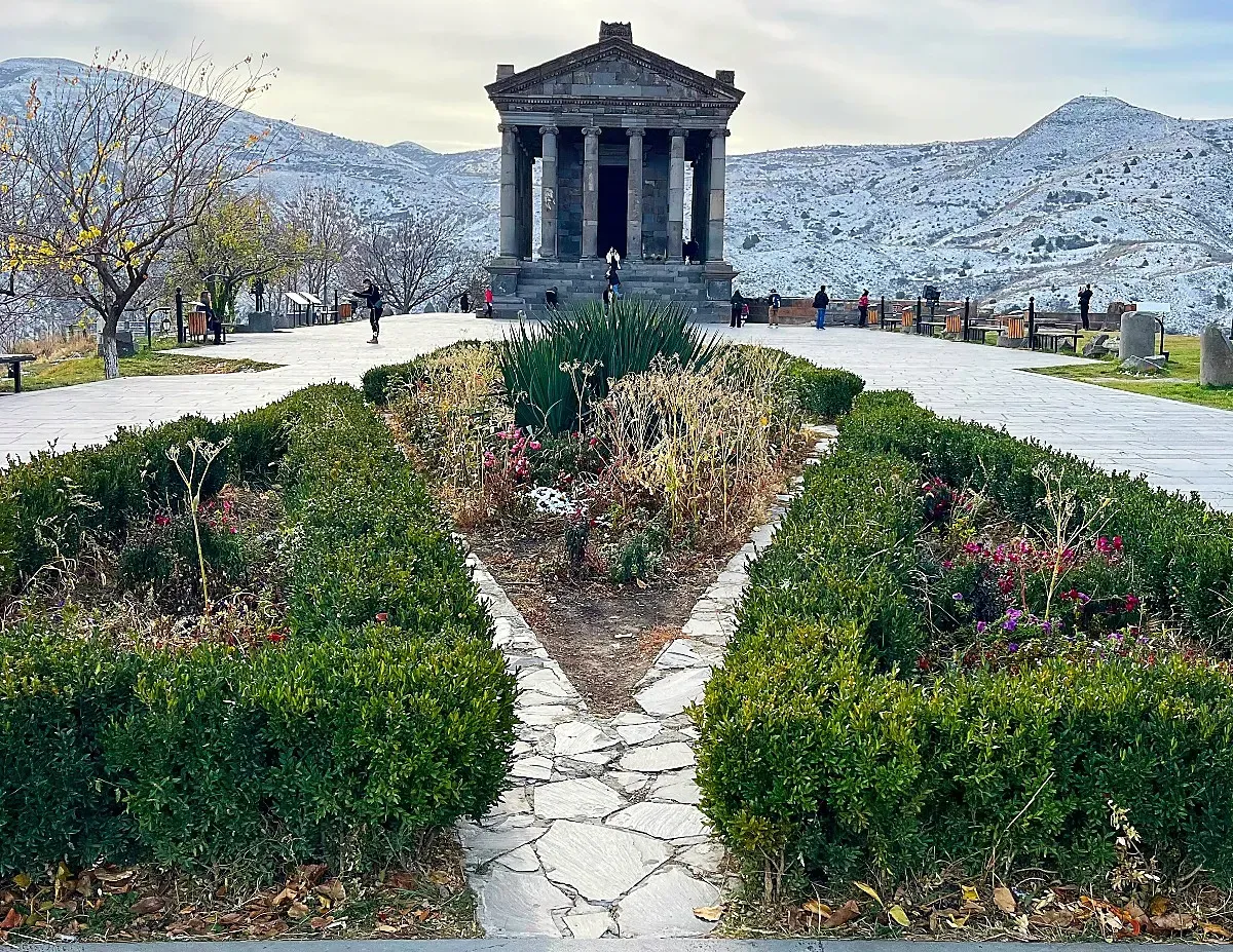 Garni Temple by Mr. Wanderer Shrubs in the foreground with a temple six-columns wide at the center with snowy mountains in the background