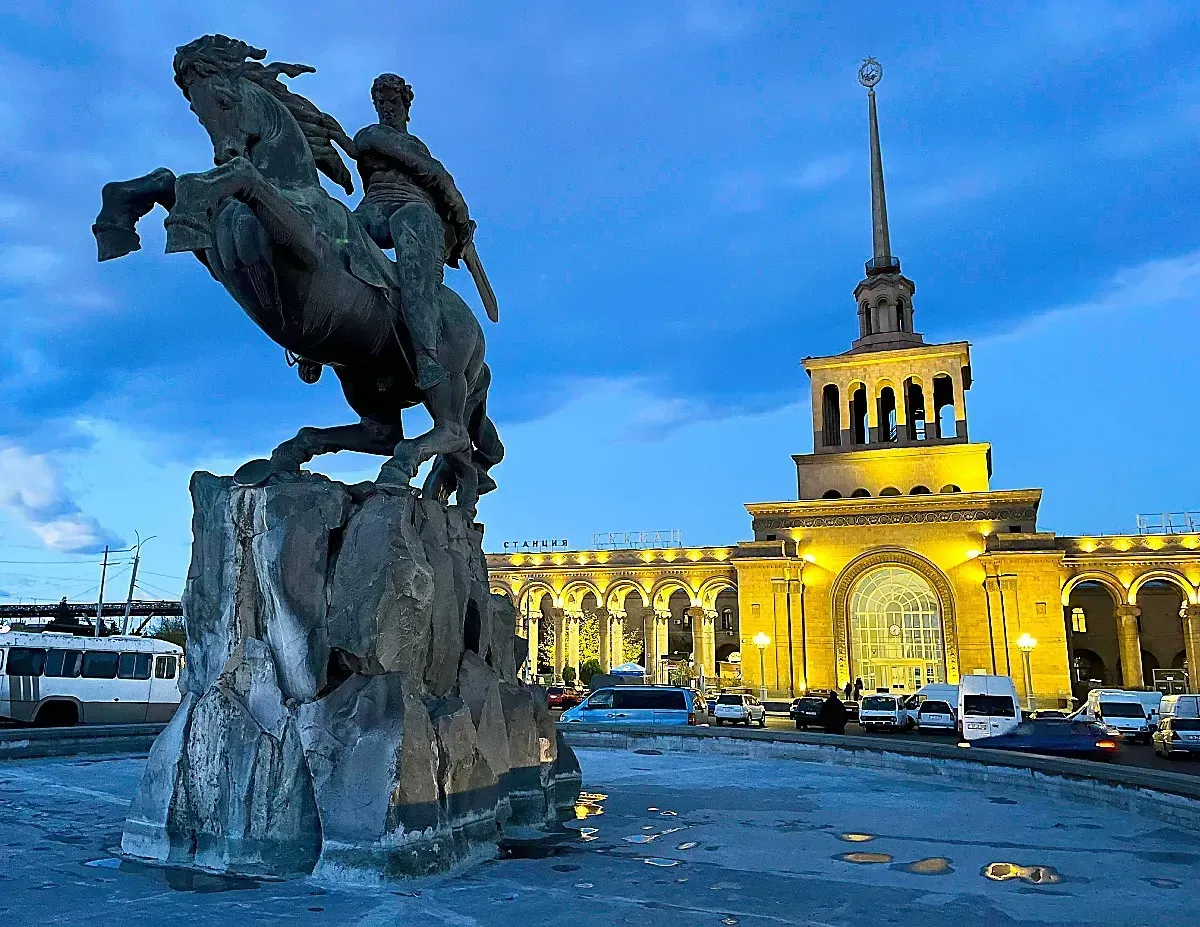 Yerevan Railway Station by Mrs. Wanderer Statue of mounted man in front of a lit-up railway station