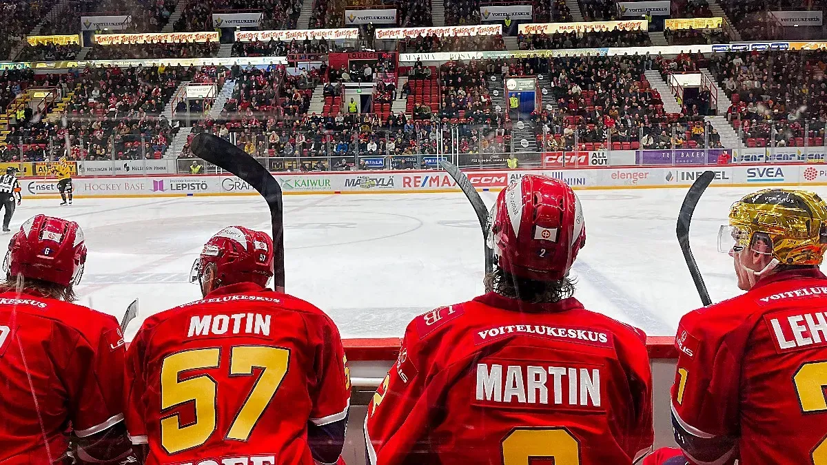 HIFK Game by Mrs. Wanderer The backs of four hockey players sitting alongside an ice rink