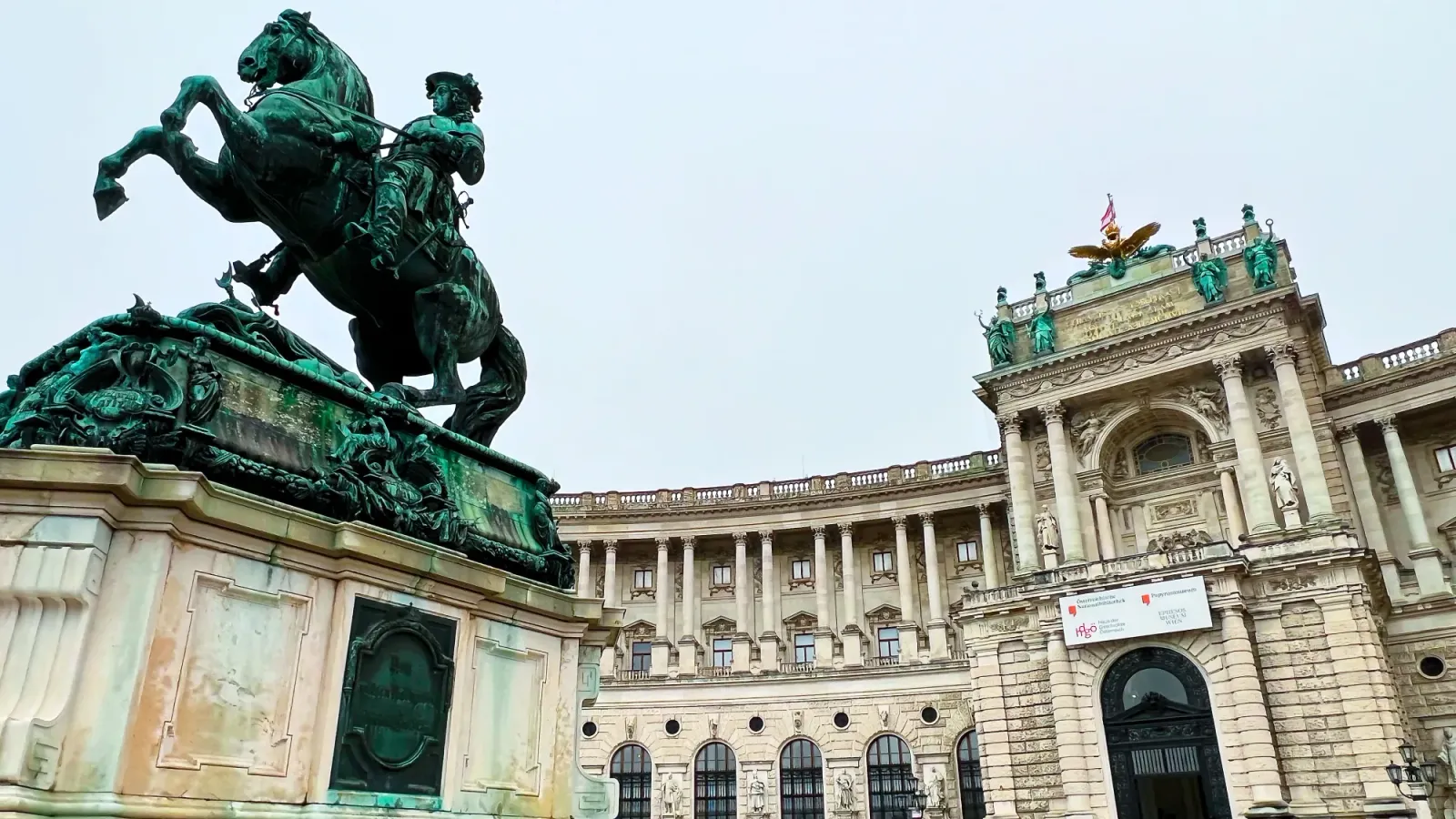 Hofburg by Mr. Wanderer Stone building with a green statue of a mounted horse in the foreground.