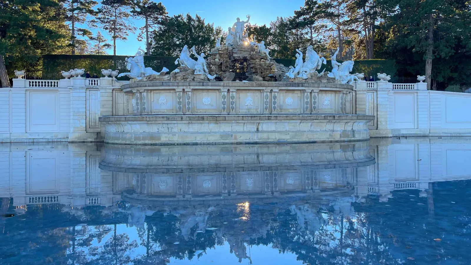 Neptune Fountain by Mrs. Wanderer Marble fountain with the sun and trees set behind it and its reflection in the ice-covered pond in front of it
