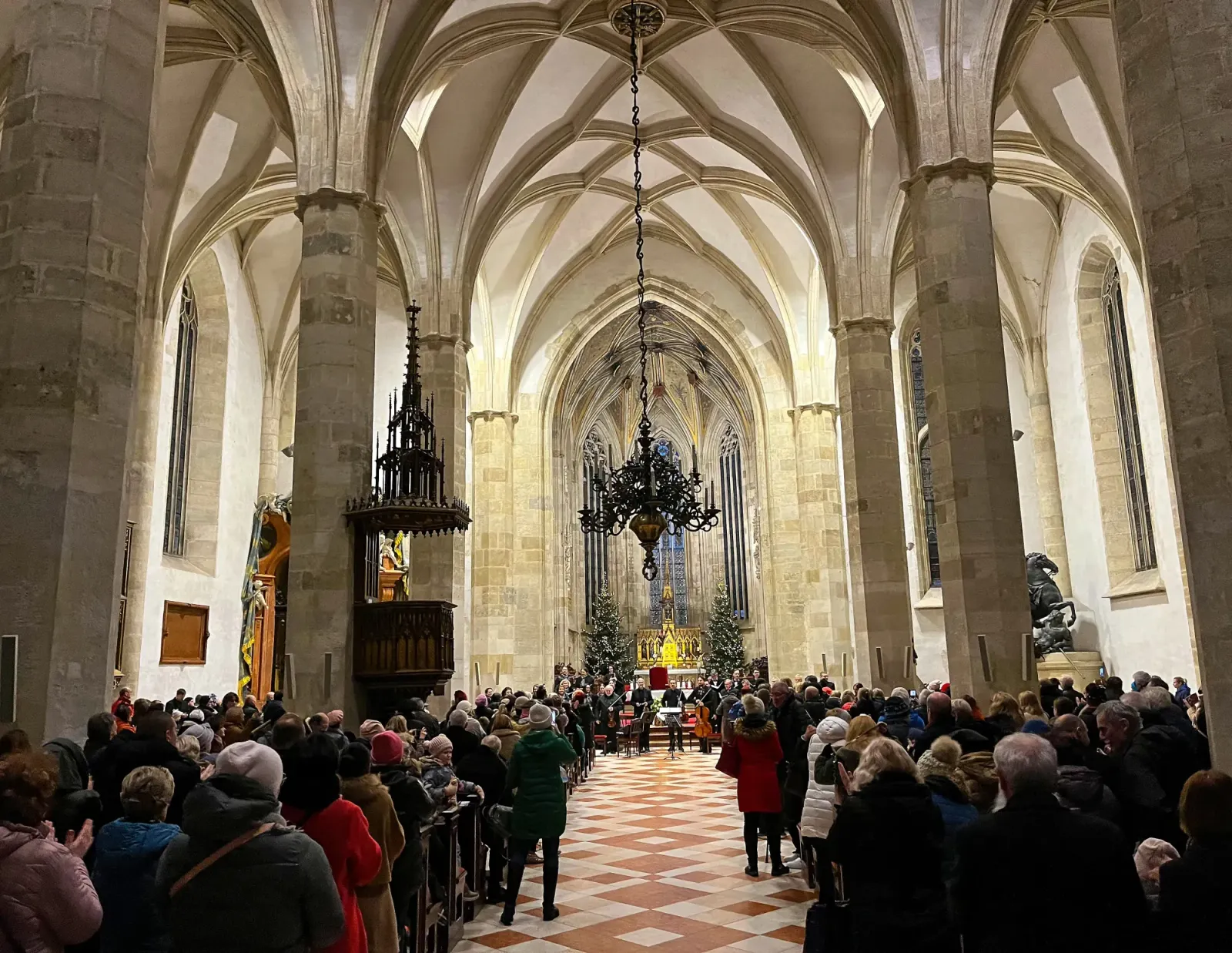 Slovakian Christmas Concert by Mr. Wanderer Arched church hall with stone flooring and packed pews with a choir at the altar