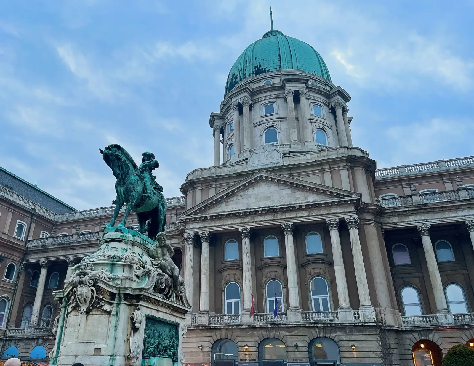Buda Castle by Mr. Wanderer Columned facade with green dome and a green horse and rider statue in front of it
