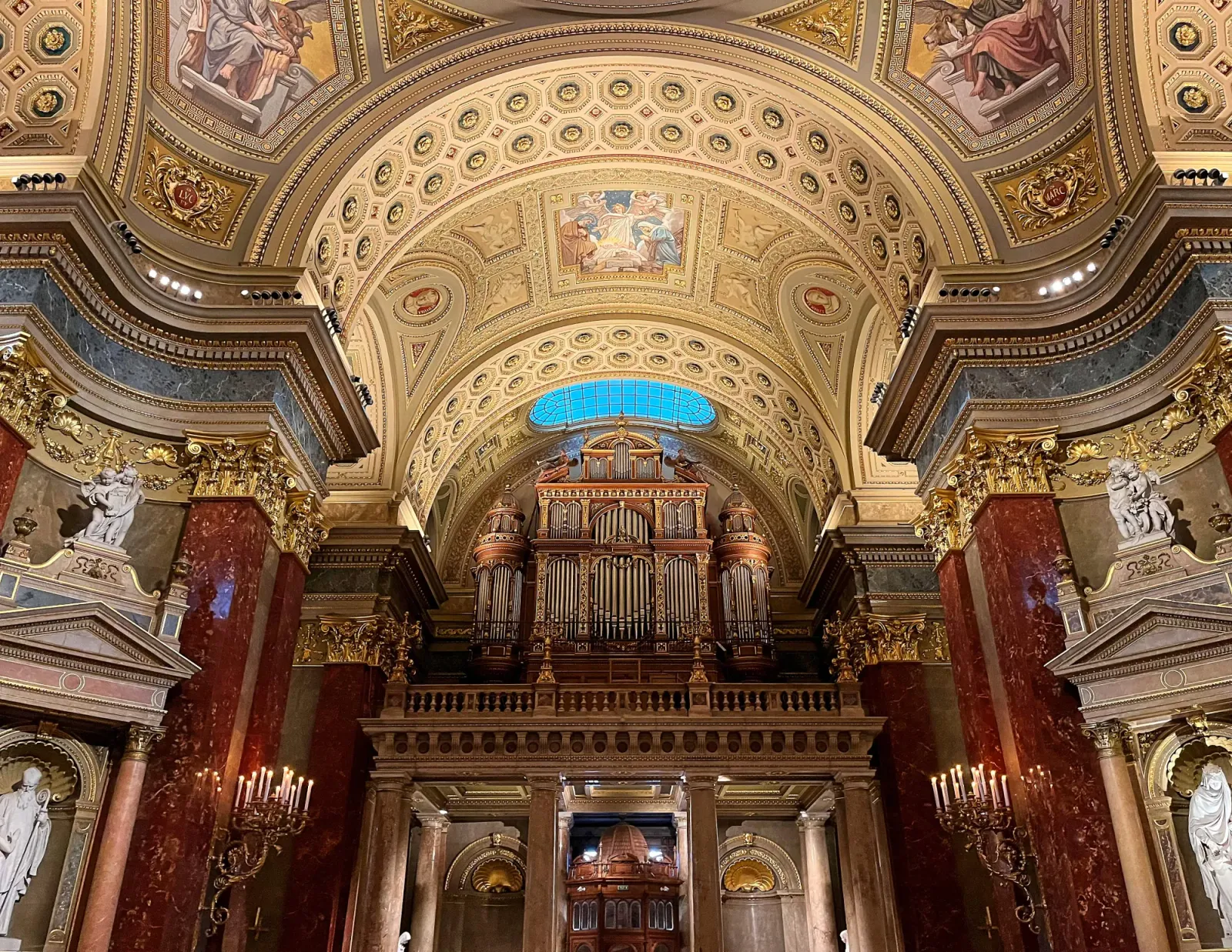 St. Stephen's Organ by Mrs. Wanderer Red marble walls and ornate wood and gold organ under a golden ceilding with paintings and floral molding.