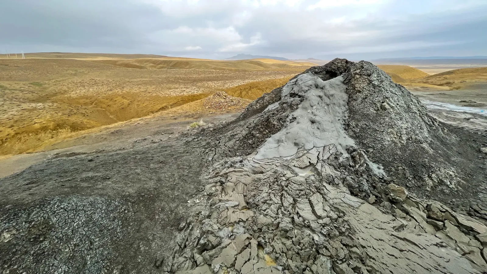 Grey mound of coagulated grey mud billowing out of the top of the volcano