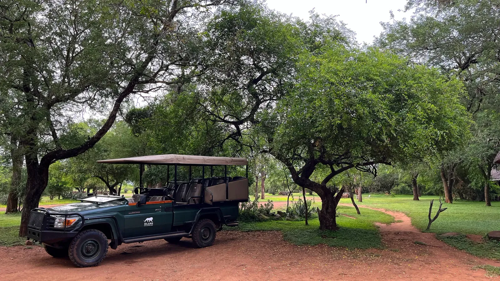Game Drive Vehicle by Mrs. Wanderer Green truck with a canvas awning sitting under trees
