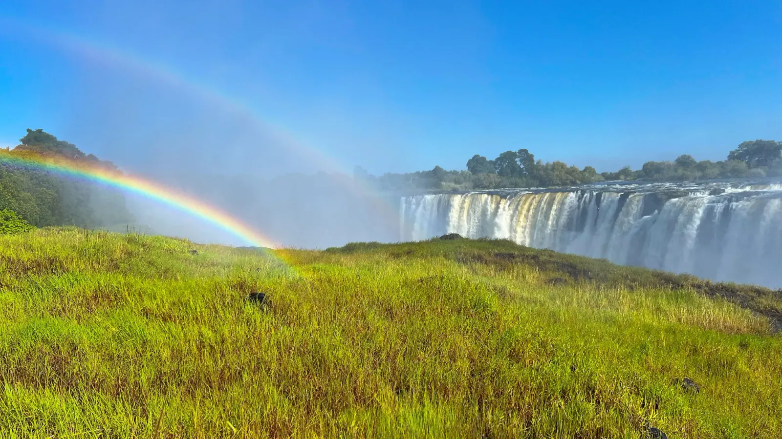 Victoria Falls Viewpoint by Mr. Wanderer Green grasses opposite the falls with a double rainbow in the mist