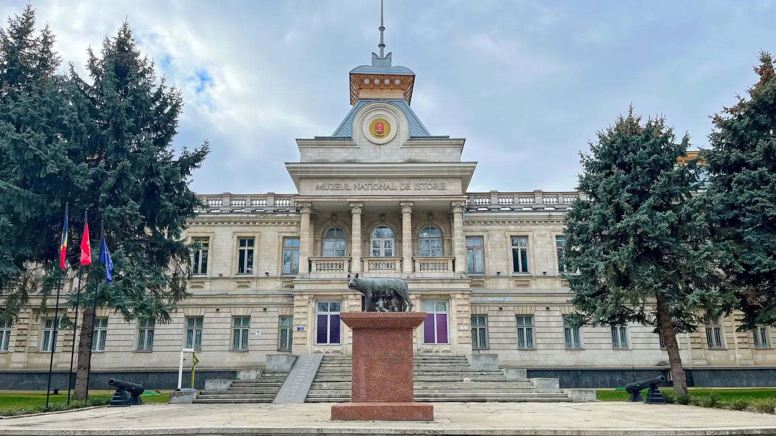 Moldovan Architecture by Mrs. Wanderer Stone building with four columns above the entry stairs and a statue of Romulus and Remus in front.