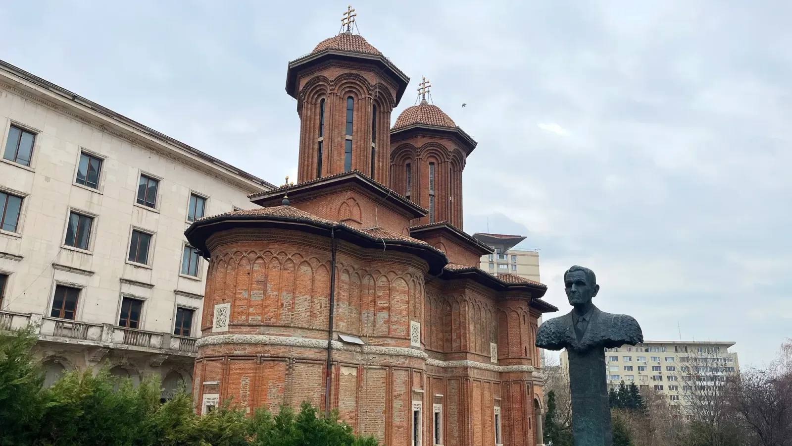 Piata Revolutiei by Mrs. Wanderer Brick steepled structure with a statue-bust in the foreground
