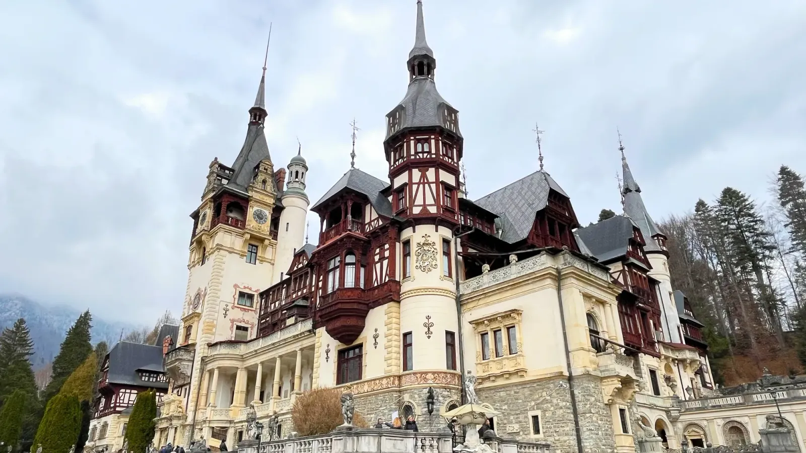 Peleș Castle by Mrs. Wanderer Stone, cream, and dark red-stained wooden castle with multiple turrets
