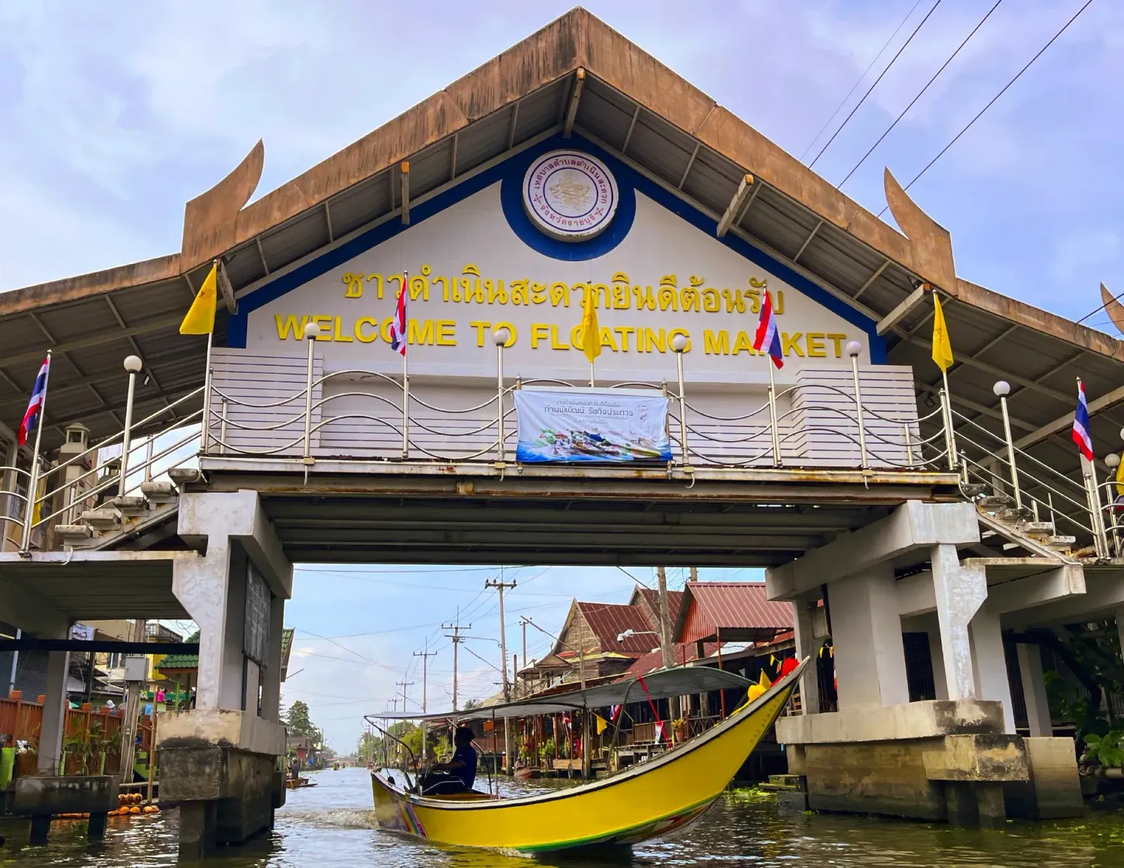 Floating Market Entrance by Mrs. Wanderer Yellow motor boat foating under walking bridge indicating the entrance to the Floating Market