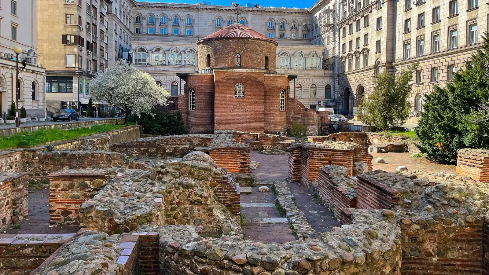 Church of St. George by Mrs. Wanderer Brick church with stone/brick ruins laying in front of it