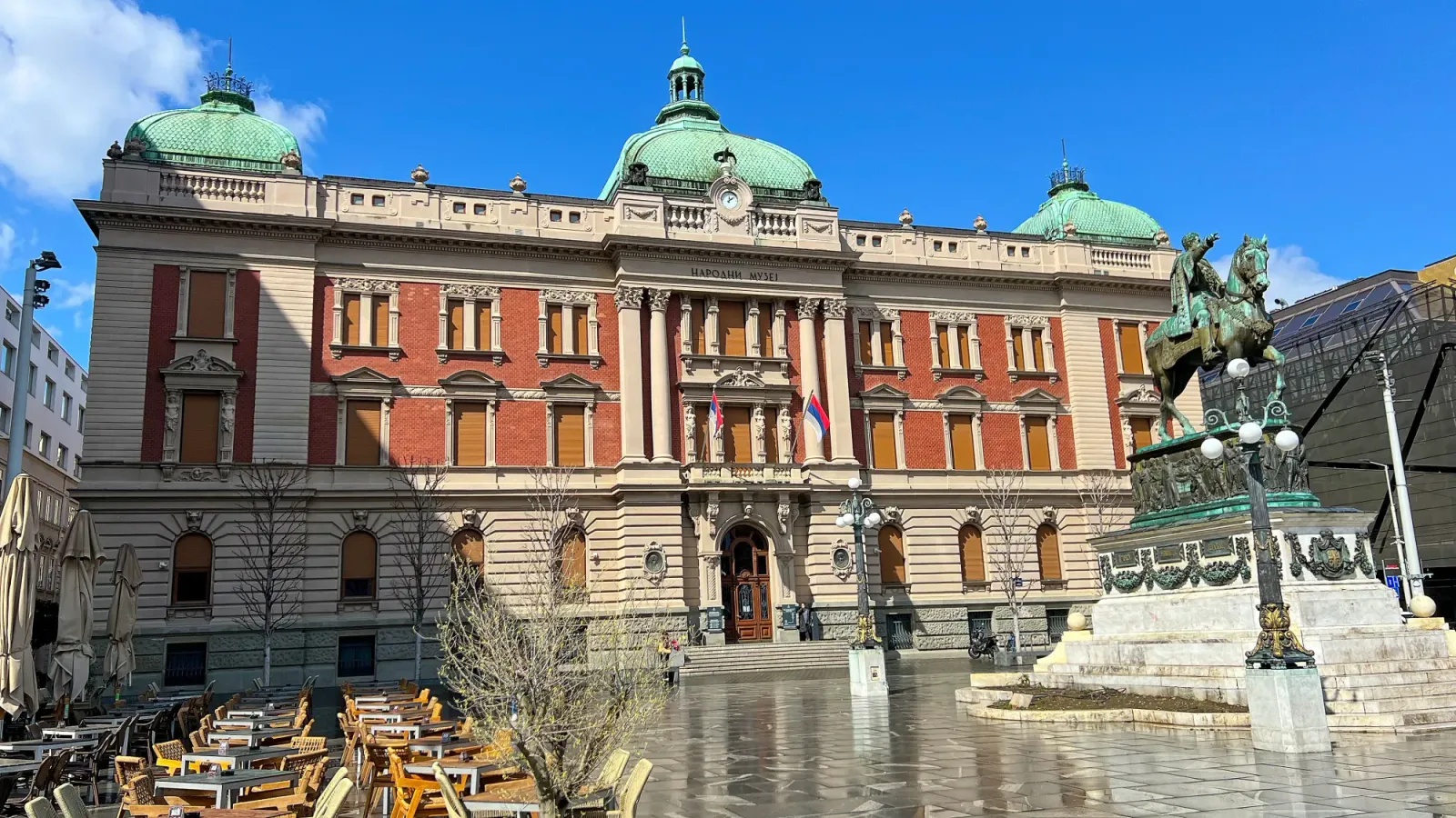 National Museum of Serbia by Mr. Wanderer Building with green tiled roof and a statue of a man riding a horse in the center of the plaza