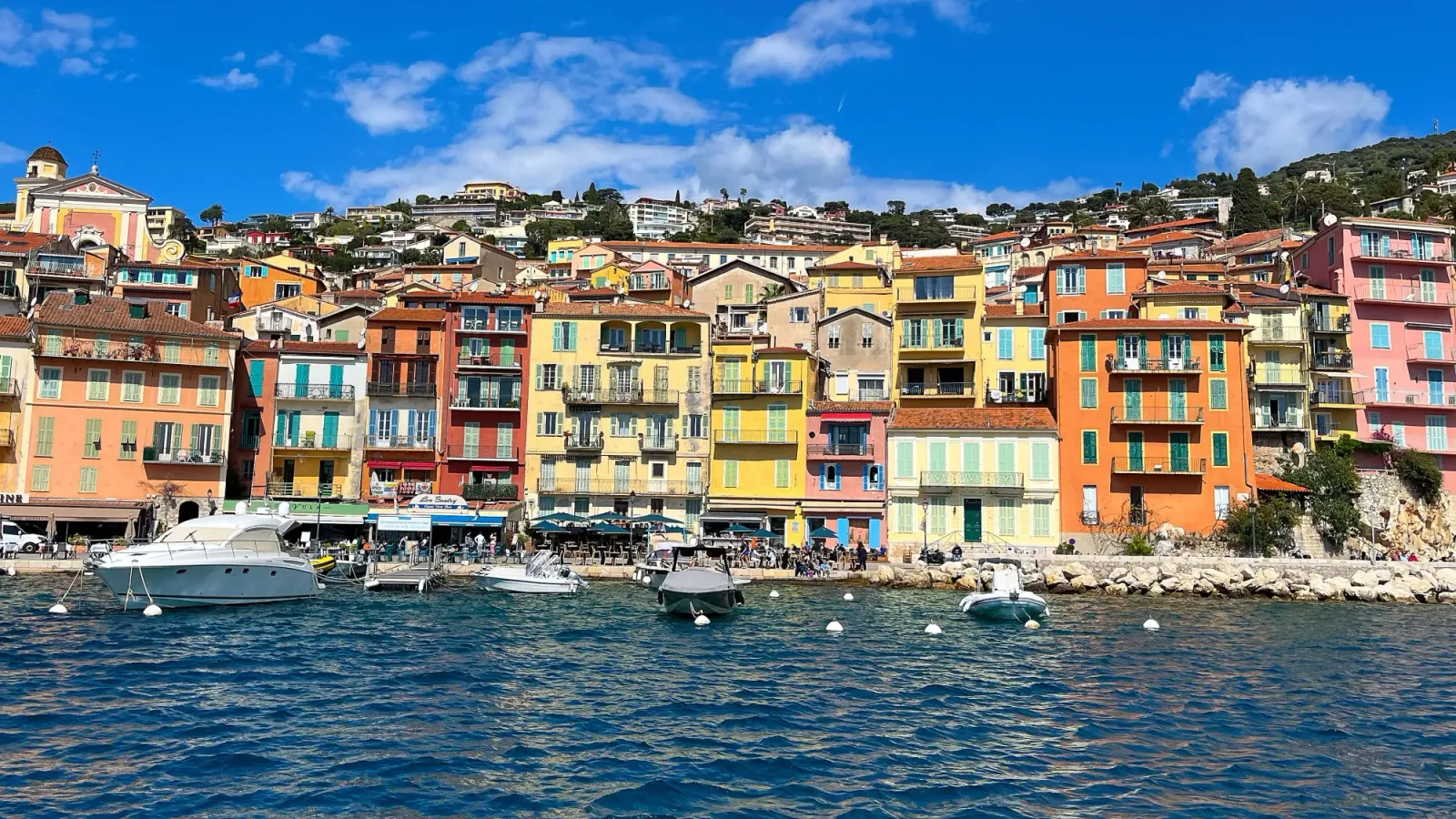 Orange, pink, and yellow buildings abutting the rocky coast lined with boats