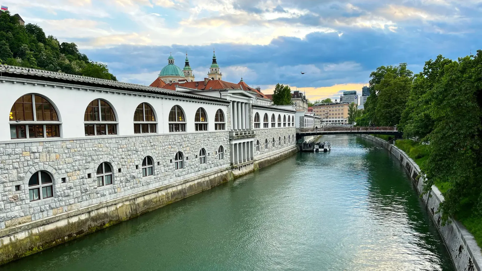Ljubljanica by Mrs. Wanderer River with a stone building abutting it and bridge crossing over it during dusk