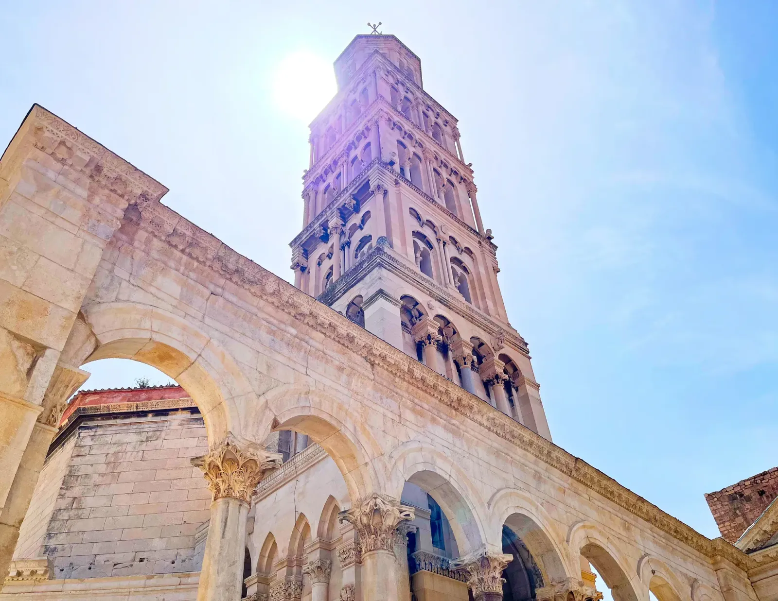 Cathedral of St. Dominus by Mrs. Wanderer Tan stone tower set against the sun with arches in front of it