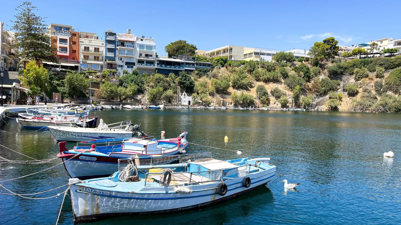 Cretan Harbor by Mrs. Wanderer Blue bay with small boats moored along its side