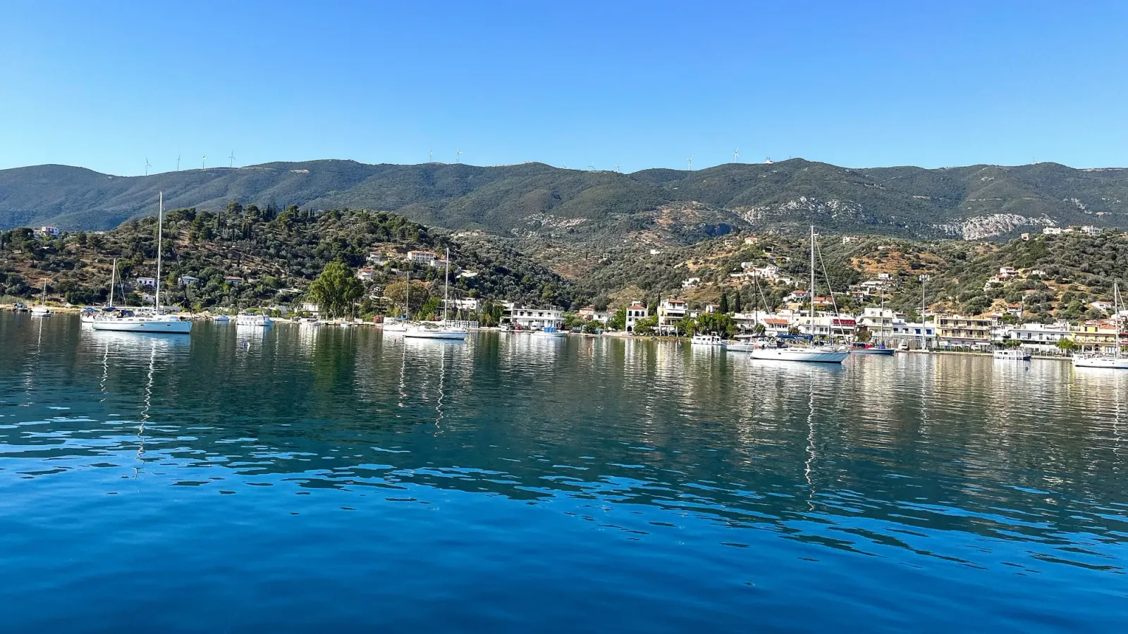 Saronic Island Lookout by Mrs. Wanderer Series of boats scattered across a blue harbor set against a green hilltop