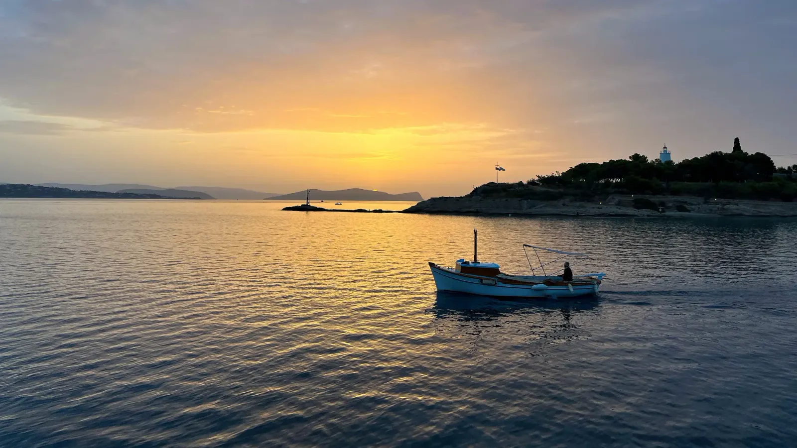 Argolic Gulf Sunsets by Mrs. Wanderer One lone boat cruising through a soft orange light as the sun sets against the edge of an island